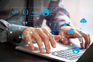 small business technology team member coding on a computer with augmented icons floating above keyboard